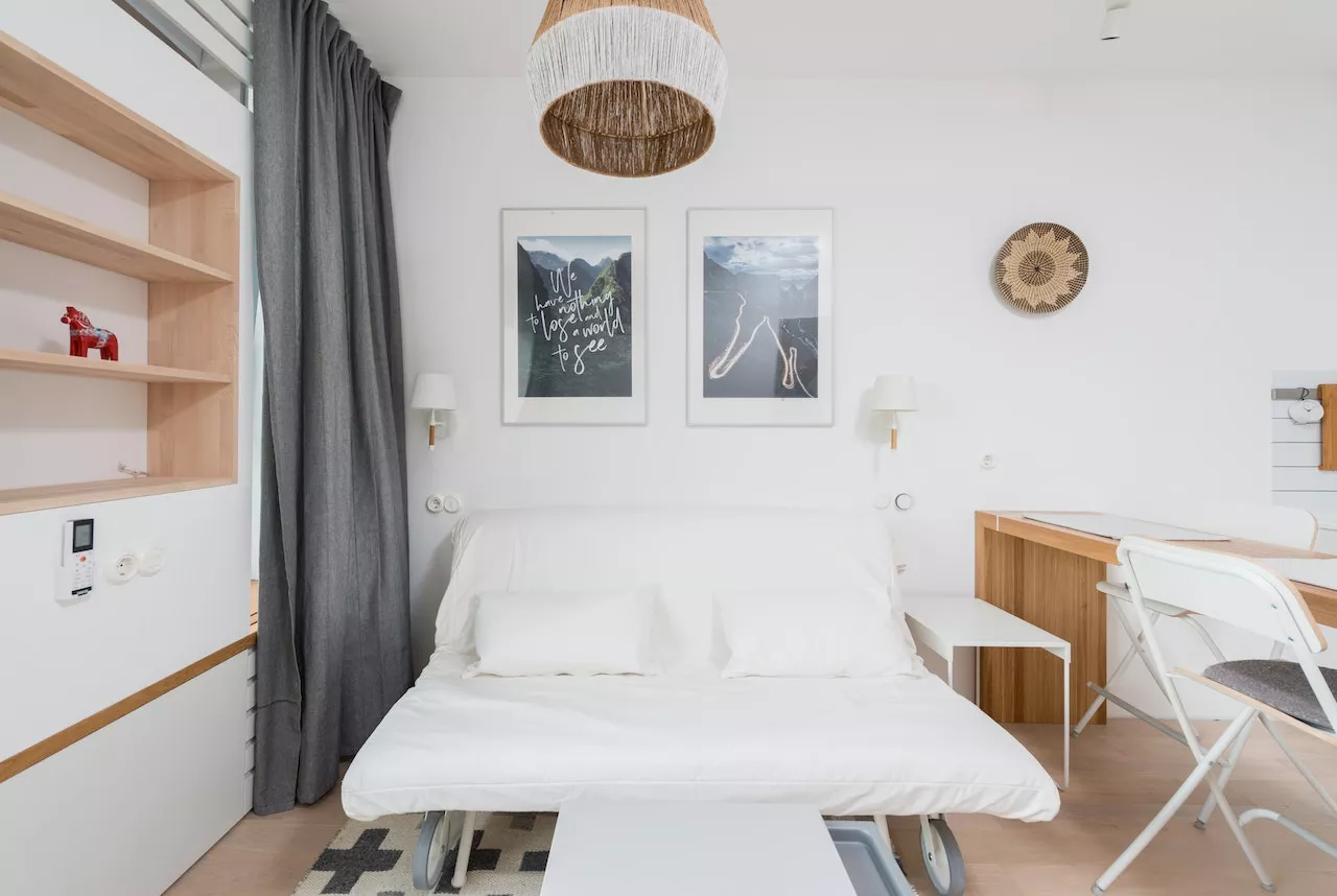 یک مبل راحتی تخت شو سفید رنگ که قابلیت تبدیل به مبل راحتی را نیز دارد این تخت هیجان انگیز در اتاقی با دیوار های سفید ، پرده طوسی رنگ قرار گرفته