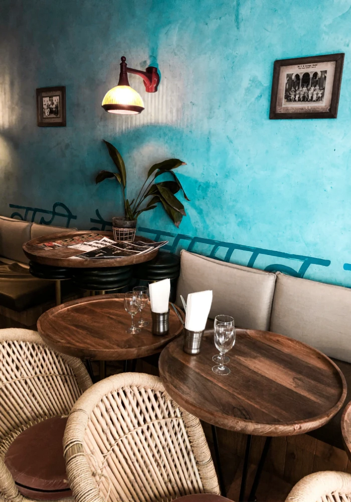 کافه که رنگ دیوار آن آبی کمرنگ میباشد و دارای مبلمان راحتی کرمی و صندلی های چوبی و میز جوبی میباشد که تابلو ها و چراغ ها به دیوار وصل هستند و لیوان ها و دستمال کاغذی بر روی میز قرار داده شده است