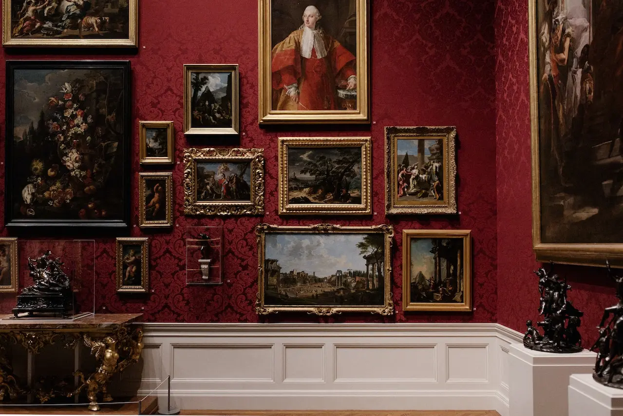 تابلو هایی نقاشی که به دیوار قرمز وصل شده است و میز سنگی نیز قرار دارد