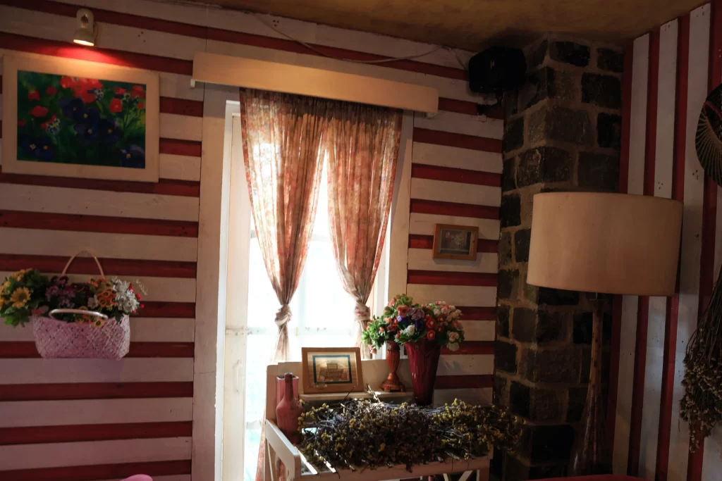 اتاقی که سبک قدیمی قرمز و سفید دارد و تابلو عکس به دیوار وصل شده است و بر روی میز نیز گل و برگه قرار دارد