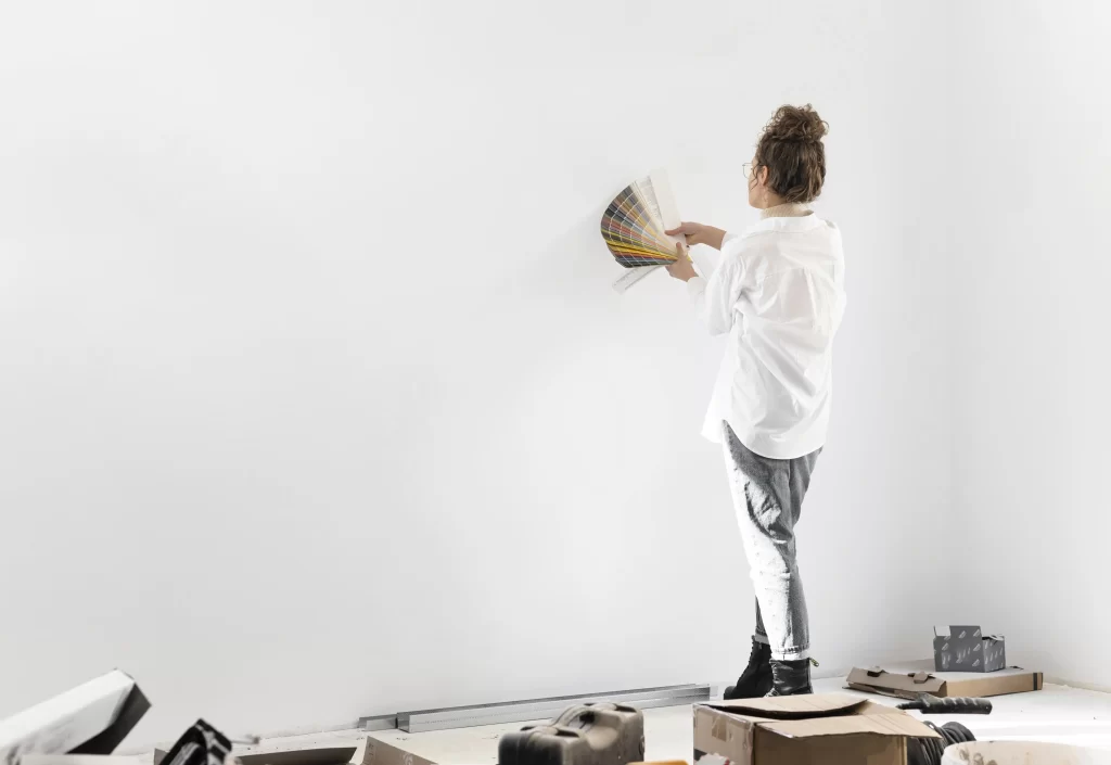 زنی که پالت رنگی در دستانش است و درحال انتخاب رنگ و دیزاین دیوار سفید رنگ جلویش میباشد