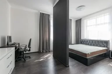 یک تختخواب بزرگ در اتاق است که این اتاق با یک دیوار نما به دو قسمت تبدیل شده و در سمت دیگر میز و صندلی برای کار جدا شده است.